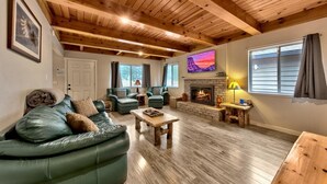 A cozy living room with a fireplace, leather sofas, wooden flooring, and a high ceiling. - Tahoe River Chalet 2782b 4 Bedroom Home (South Lake Tahoe)