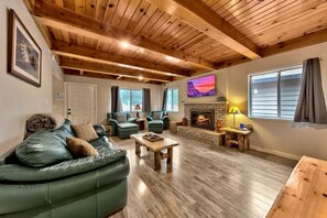 A cozy living room with a fireplace, leather sofas, wooden flooring, and a high ceiling. - Tahoe River Chalet 2782b 4 Bedroom Home (South Lake Tahoe)