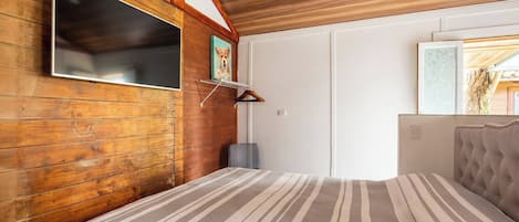 A room with wooden walls, a large flat-screen TV mounted on the wall, a striped rug, and a tufted headboard.