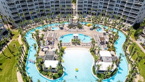 Un hotel grande, de varios niveles, con una piscina central rodeada de palmeras y tumbonas.