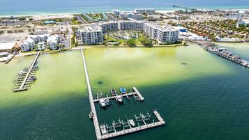 An aerial view of a marina with multiple docks and boats, surrounded by a resort complex with several buildings and a beach in the background.