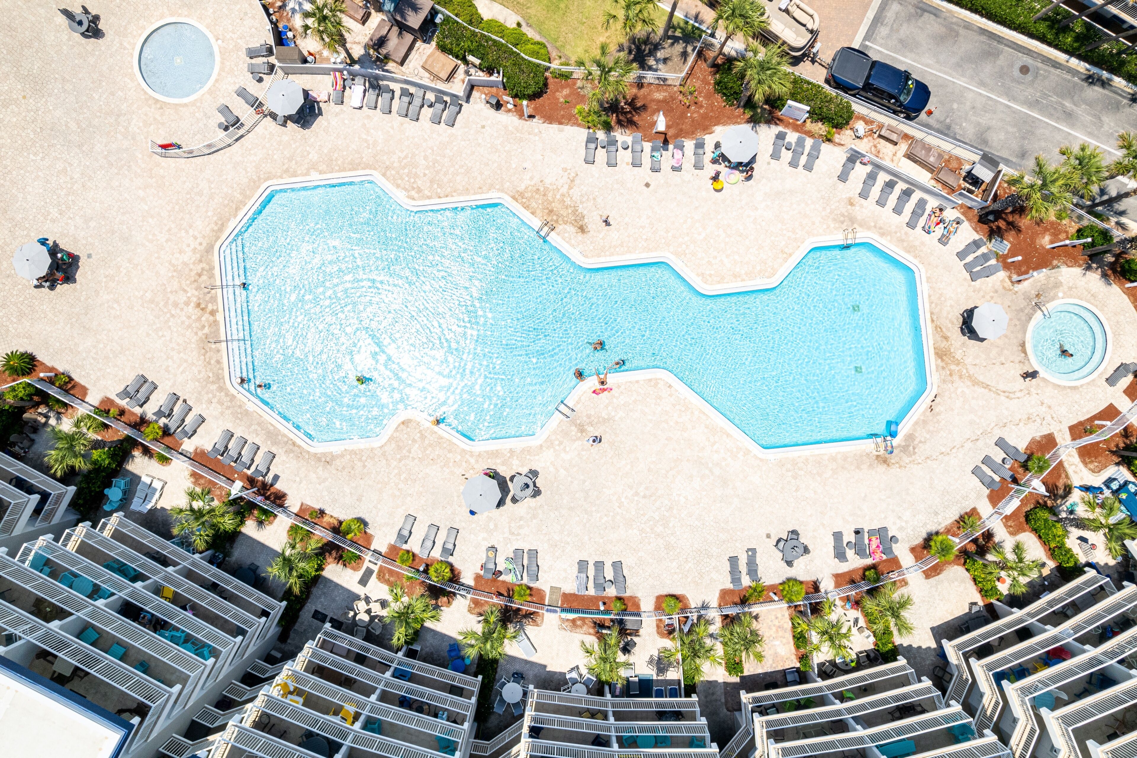 An aerial view of a hotel with a large pool, sun loungers, and palm trees.