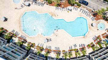 An aerial view of a hotel with a large pool, sun loungers, and palm trees.