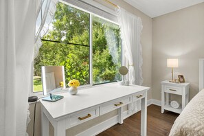 A bedroom with a large window, a bedside table with a lamp, and a dresser with drawers. - Arlington Park Oasis 4 Bedroom Home (Sarasota)