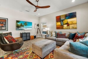 A modern living room with a ceiling fan, a large painting, a television, and a patterned rug. - Arlington Park Oasis 4 Bedroom Home (Sarasota)