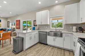 A modern kitchen with white cabinets, a stainless steel sink, and a wooden floor. - Arlington Park Oasis 4 Bedroom Home (Sarasota)