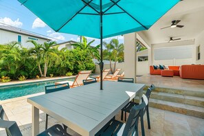 A poolside area with a table and chairs, a covered umbrella, and a sofa. - Arlington Park Oasis 4 Bedroom Home (Sarasota)