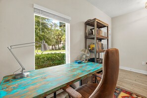 A room with a wooden desk, a leather chair, a bookshelf, and a window with a view of greenery. - Arlington Park Oasis 4 Bedroom Home (Sarasota)