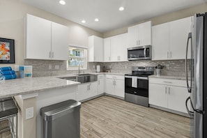 A modern kitchen with white cabinets, a stainless steel refrigerator, a microwave, and an oven. - Arlington Park Oasis 4 Bedroom Home (Sarasota)
