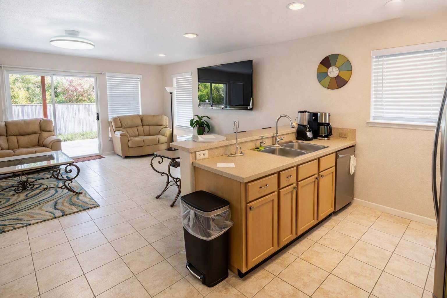 A compact living space with a kitchenette, a sofa, a coffee maker, and a trash bin.