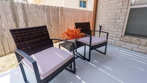 Un patio con dos sillas, una mesa, una cerca de madera y un muro de ladrillo.