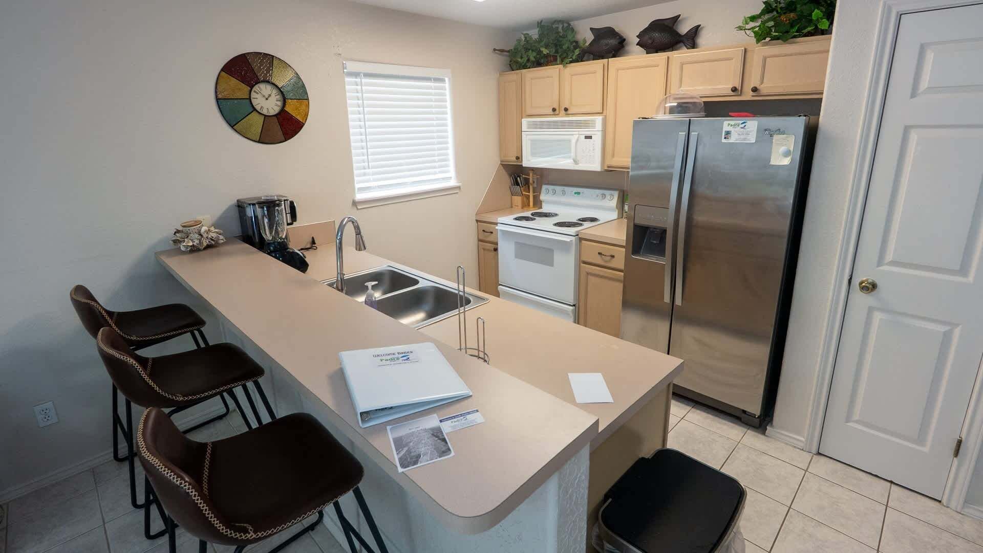 A kitchen with a central island, stainless steel appliances, and a clock on the wall.