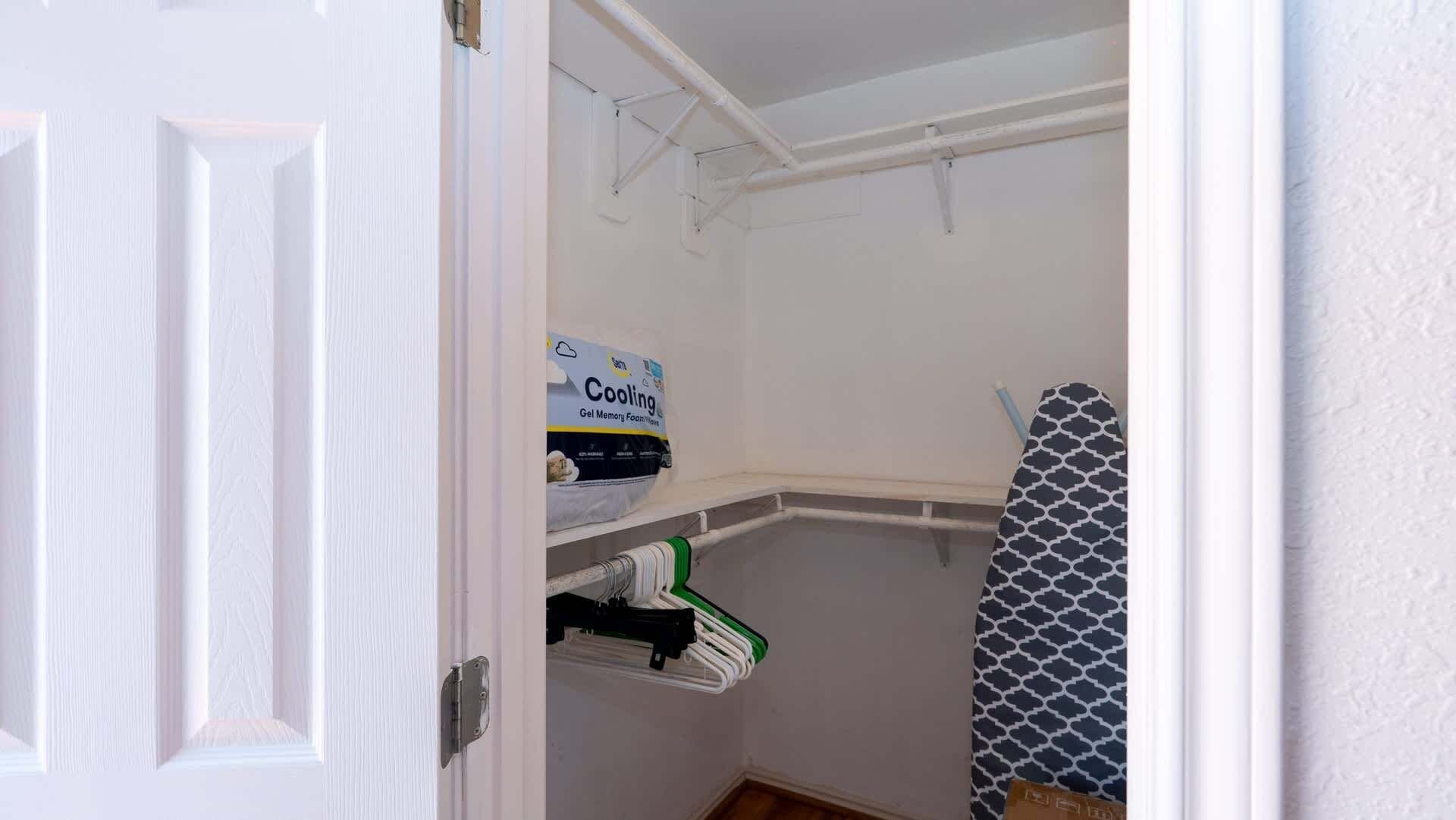 A small, white-walled room with a white door, a drying rack, and a box labeled 'Cooling Gel Memory Foam Movers.'