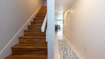 Una scala con gradini in legno che conduce a un piano superiore, un corridoio con un tappeto decorato e una porta in fondo.
