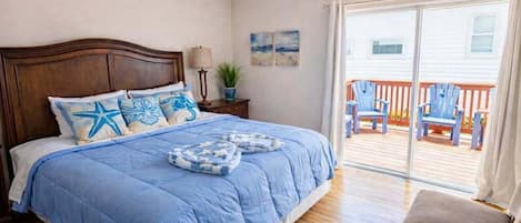 A bedroom with a large bed, a wooden headboard, a nightstand, a lamp, and a view of a deck with chairs.