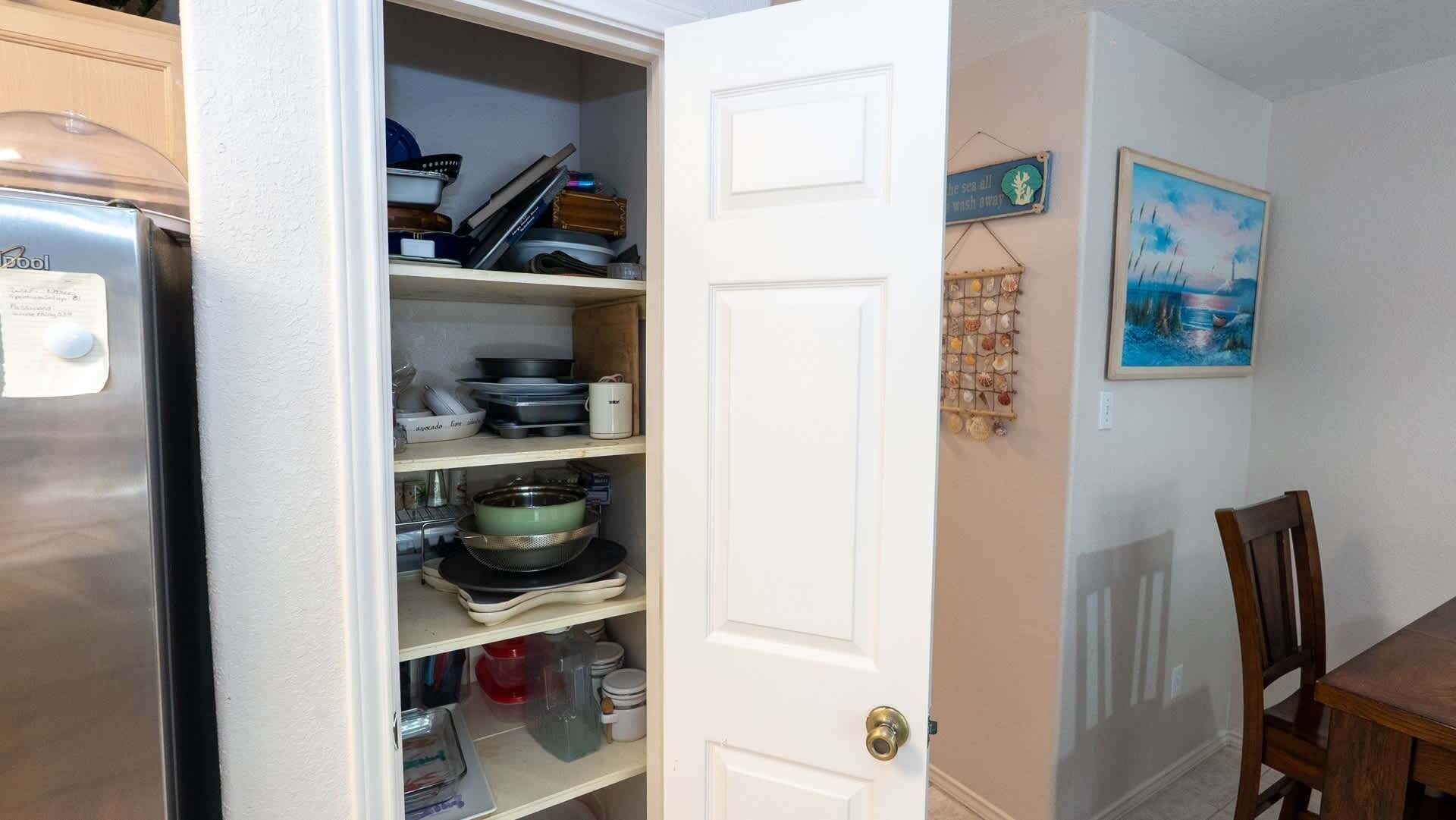 A kitchen with open cabinets, a refrigerator, and a dining area with a table and chairs.