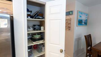 A kitchen with open cabinets, a refrigerator, and a dining area with a table and chairs.
