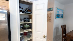 Una cocina con armarios abiertos, un refrigerador y una zona de comedor con mesa y sillas.