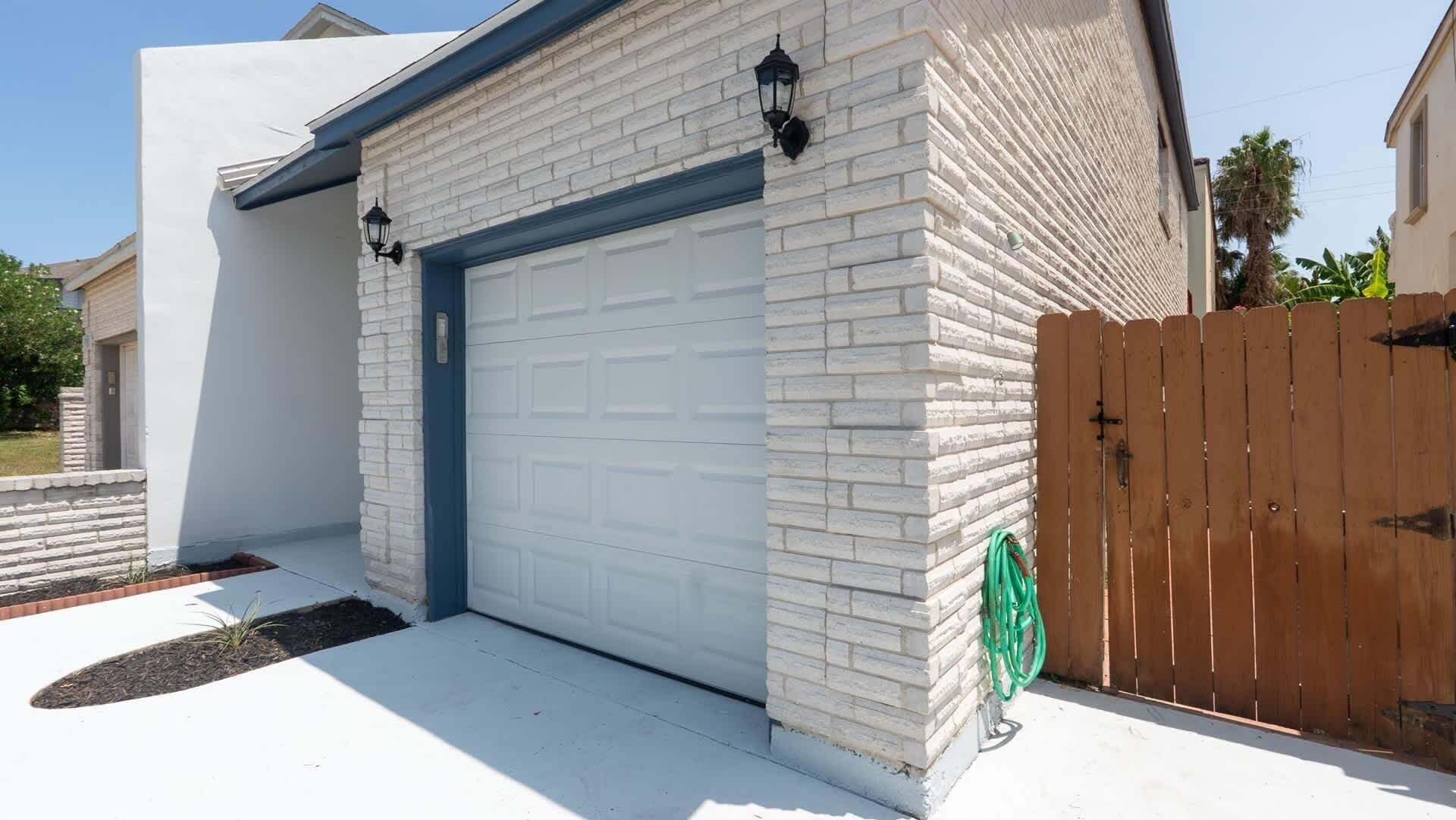 Un garaje residencial con puerta blanca, fachada de ladrillo y valla de madera.
