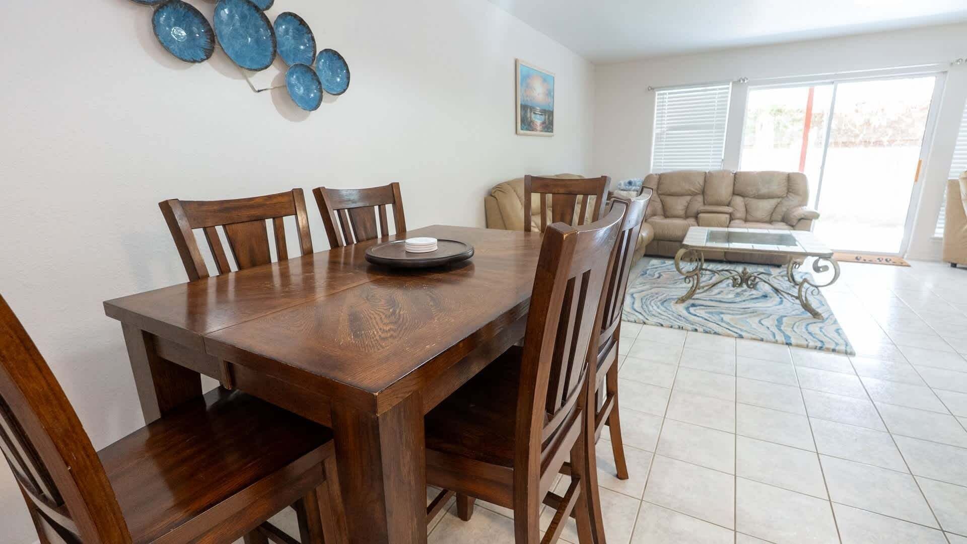 Un comedor con una mesa y sillas de madera, un adorno azul en la pared y un cuadro colgado.