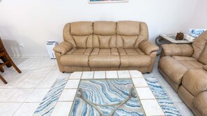 Un salón con un sofá color beige, un tapete estampado y una mesita con una lámpara.