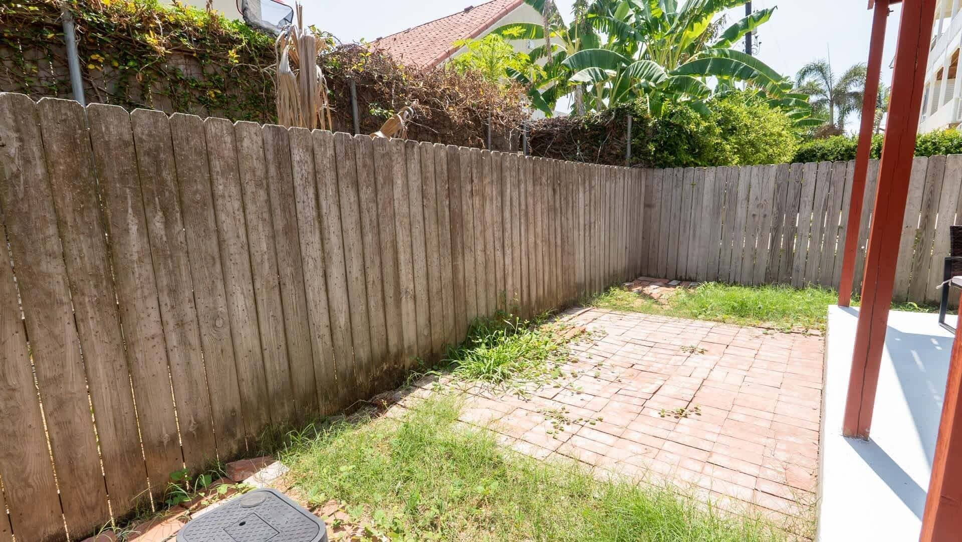 A fenced backyard with a brick patio and a manhole cover.