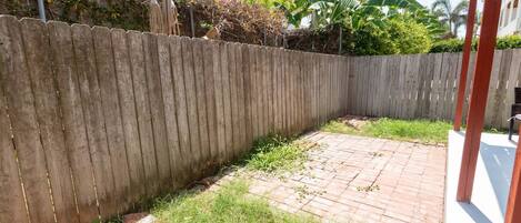 A fenced backyard with a brick patio and a manhole cover.
