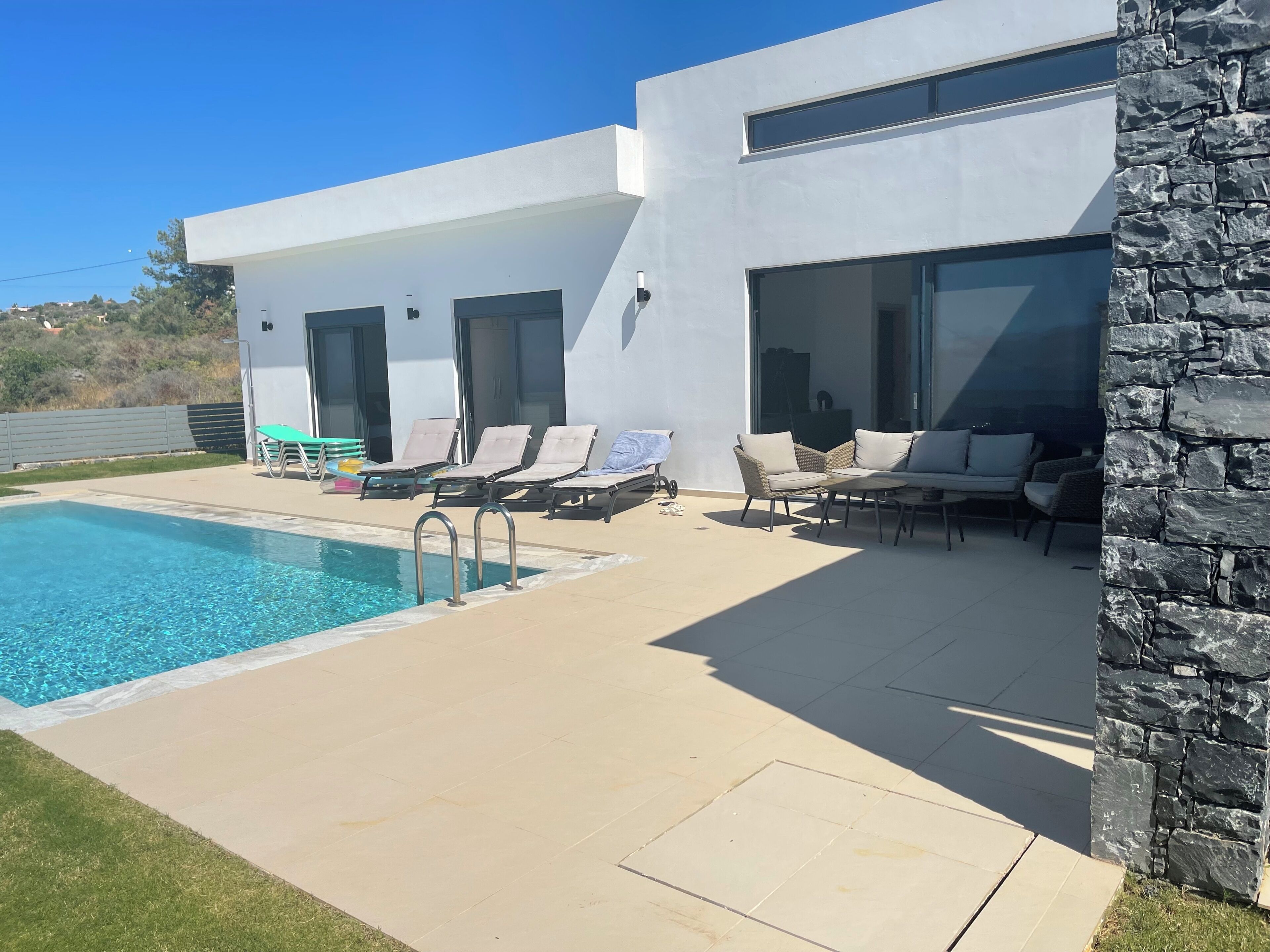 Un edificio moderno con piscina, area salotto esterna e un muro in pietra.