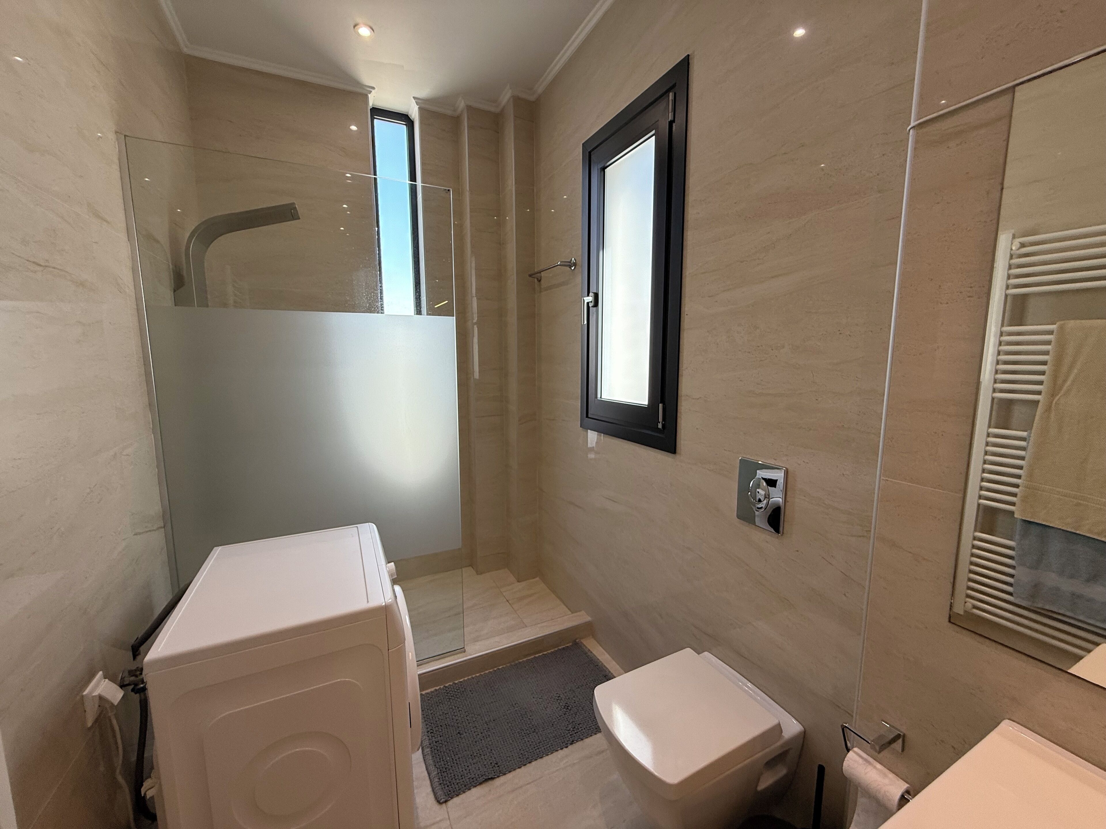 Un baño moderno con cabina de ducha de vidrio, un inodoro y un toallero empotrado.