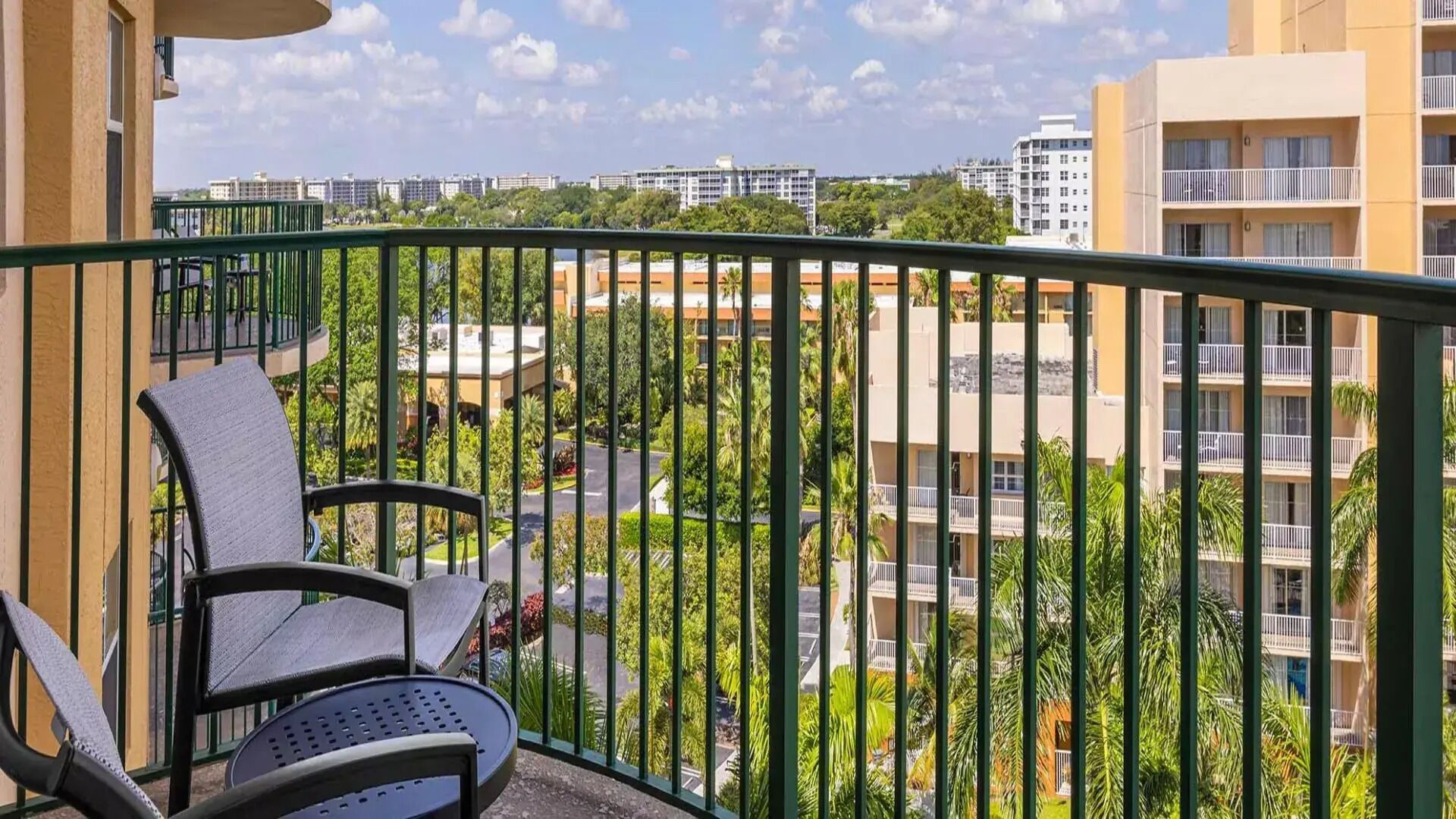 Ein Balkon mit Blick auf ein Wohngebiet, darunter ein Gebäude mit mehreren Balkonen und einem klaren Himmel.