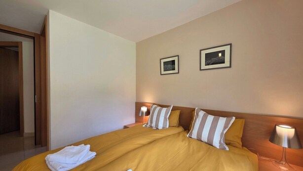 A hotel room with a large bed, two bedside tables with lamps, and two framed pictures on the wall. - Cornelia 11 Appartement/Fewo 6-Bettwohnung by Interhome (Saas-Fee)