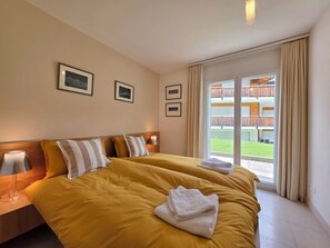 Ein Hotelzimmer mit einem großen Bett, zwei Nachttischen mit Lampen und Blick auf einen Balkon mit Holzgeländern.