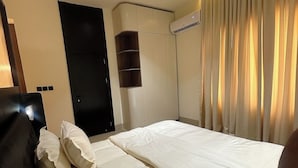 Une chambre d’hôtel avec un lit, une armoire, un miroir et une fenêtre avec des rideaux.