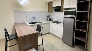 Une cuisine moderne avec une table à manger en bois, des chaises noires, une cuisinière encastrée et un réfrigérateur en acier inoxydable.