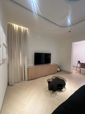 A modern living room with a flat-screen TV, wooden cabinet, and a dining area with a table and chairs.