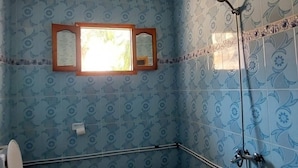 A bathroom with patterned walls, a toilet, a shower, and a window. - Beautiful house near the beach (Axdir)