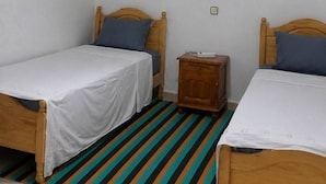 A room with two wooden beds, a striped rug, a small wooden nightstand, and a ceiling light fixture. - Beautiful house near the beach (Axdir)