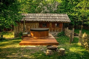 Ein rustikales Holzhäuschen mit Whirlpool davor, umgeben von einer Holzterrasse und einem Holzzaun.