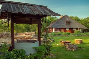 A rustic house with a thatched roof, surrounded by a garden with a wooden bench and a tree stump. - Holiday apartment in Stawki with sauna (Stawki)