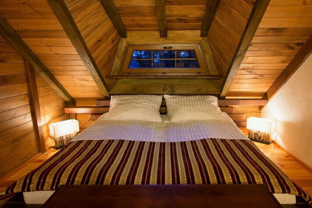 Una habitación acogedora con techo de madera, una ventana, una cama con colcha a rayas y lámparas de noche.