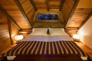 Ein gemütliches Zimmer mit Holzbalkendecke, einem Fenster, einem Bett mit gestreifter Bettdecke und Nachttischlampen.