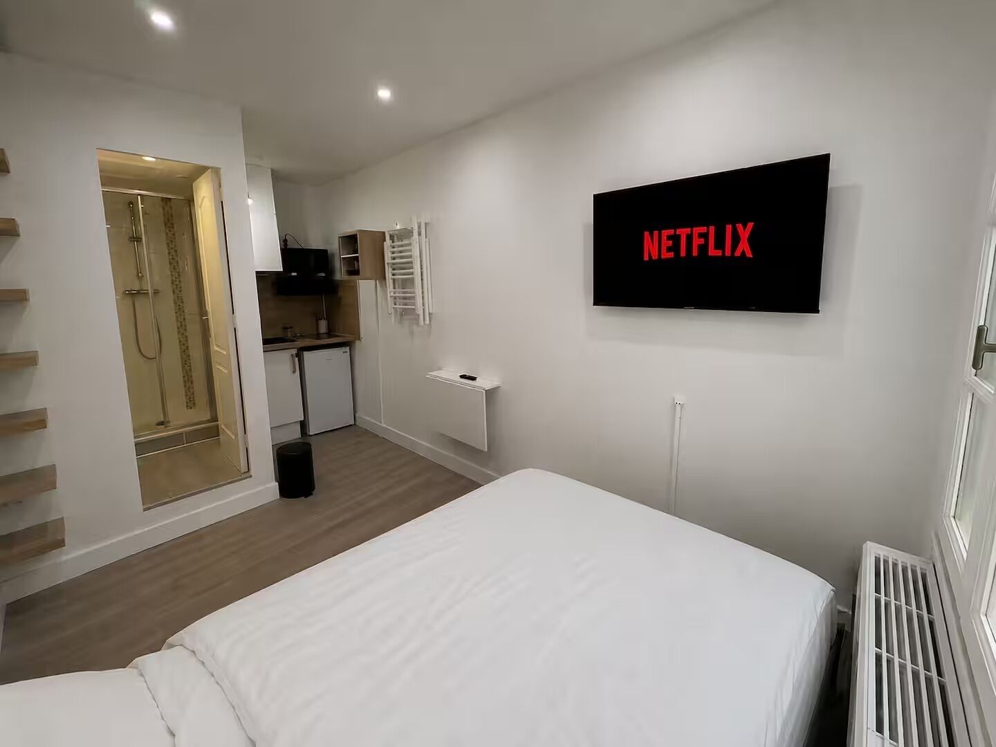 Une chambre d’hôtel équipée d’un lit, d’une kitchenette, d’une douche et d’un téléviseur fixé au mur, sur lequel apparaît le logo de Netflix.