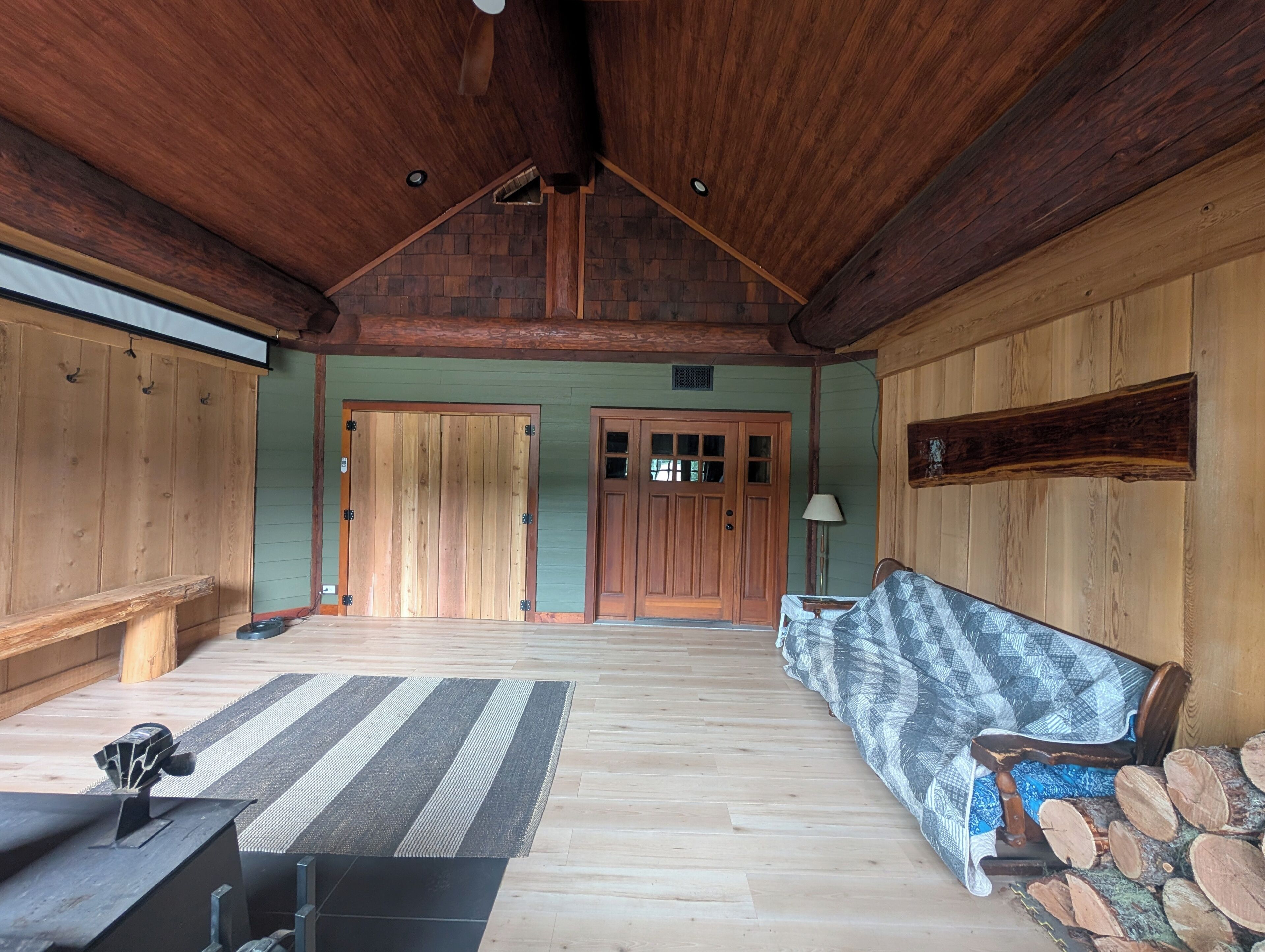 A spacious room with a wooden ceiling, a large door, a bench, and a patterned rug.