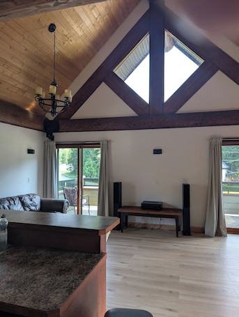 A spacious room with a high ceiling, wooden beams, a chandelier, a large table, and a sofa.