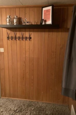 Una habitación con paredes de paneles de madera, un perchero y una estantería con recipientes metálicos.