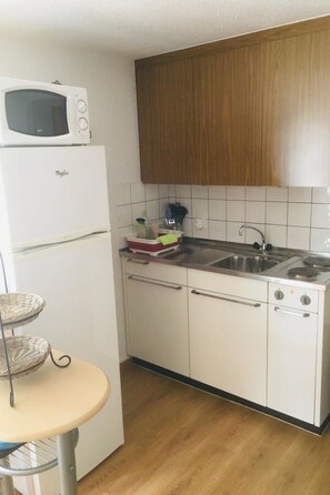 A compact kitchen with a microwave, stove, and sink. - Chalet Louise Appartement/Fewo, Dusche, WC, 1 Schlafraum 2-Zimmerwohnung by Interhome (Adelboden)