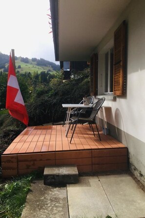 Une terrasse avec une table et des chaises, un drapeau et une vue sur un paysage verdoyant.