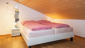 A bedroom with a sloped ceiling, a bed with checkered bedding, a bedside table with a lamp, and a wall-mounted light fixture. - Studio Zentrum OG Appartement/Fewo, Dusche, WC, 1 Schlafraum Studio by Interhome (Adelboden)