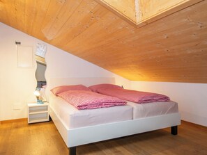 A bedroom with a sloped ceiling, a bed with checkered bedding, a bedside table with a lamp, and a wall-mounted light fixture. - Studio Zentrum OG Appartement/Fewo, Dusche, WC, 1 Schlafraum Studio by Interhome (Adelboden)