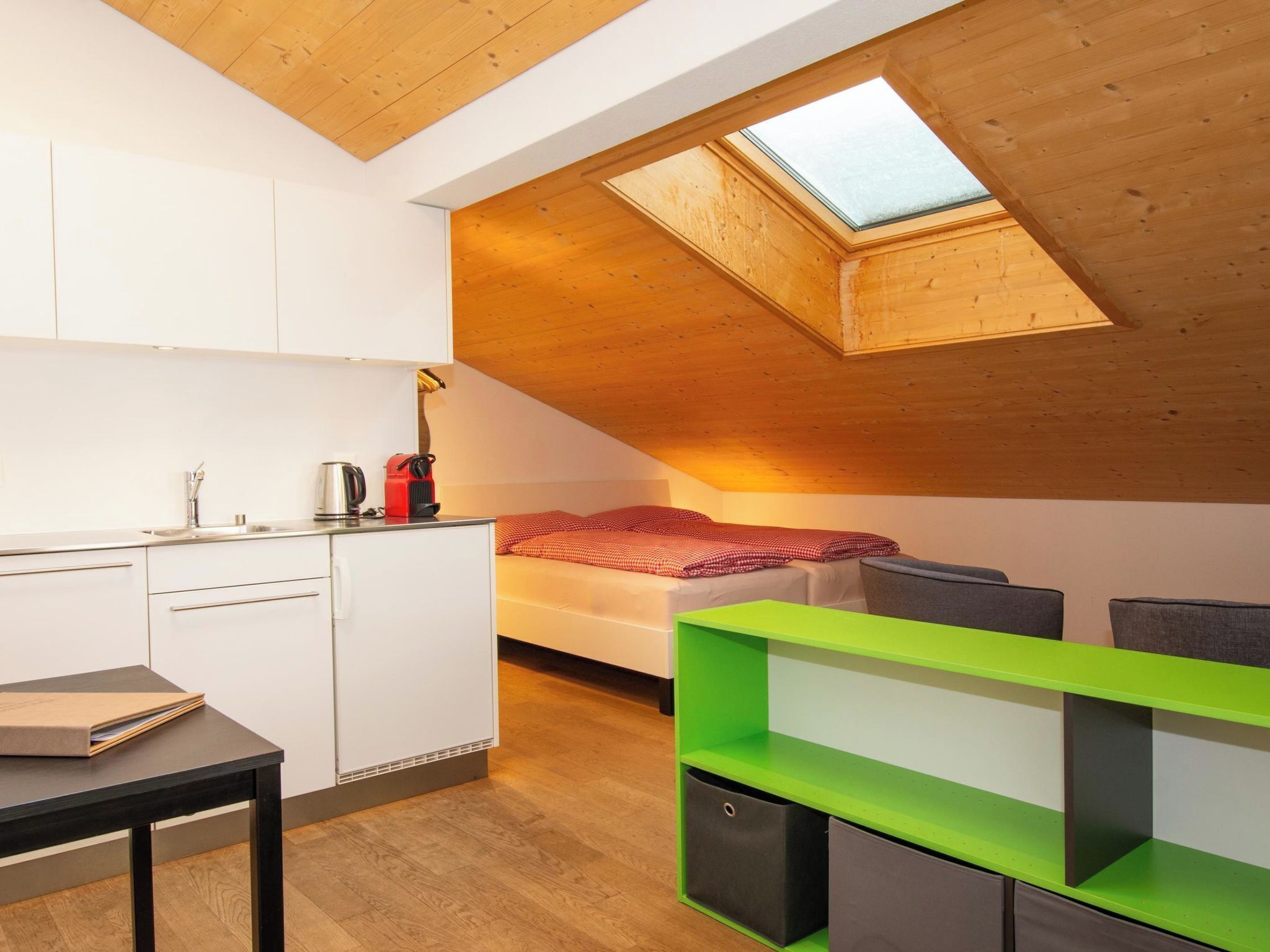 Une pièce compacte comprenant un coin cuisine, un lit et une lucarne.